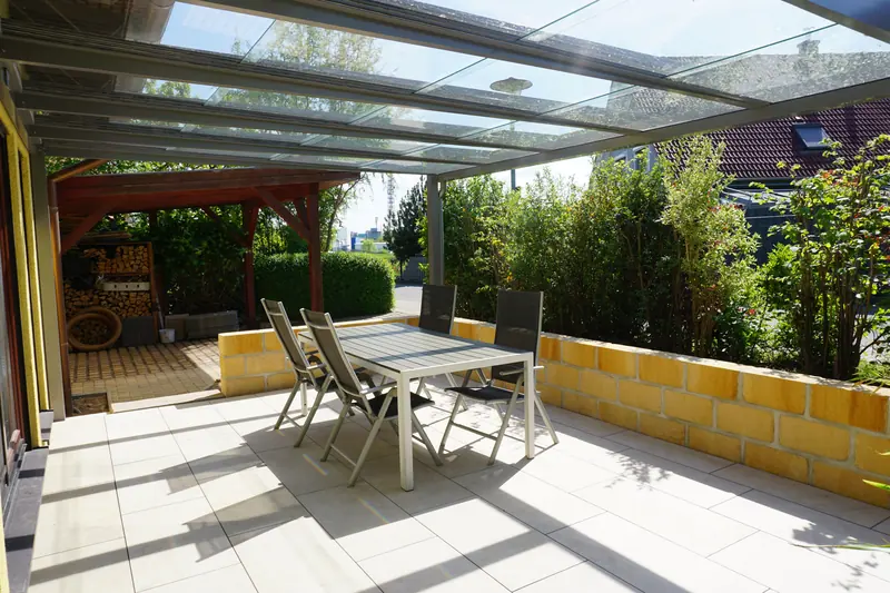 Fertige Terrasse mit hellen Platten, Sandsteinmauer und Glasüberdachung, gebaut von Moor Bau in Moritzburg